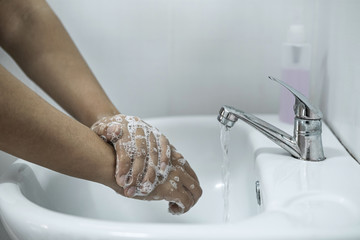 Woman washing hands under the water tap in bathroom with using soap gel for cleaning and prevention inflection coronavirus