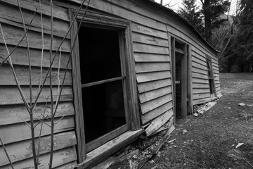 The empty windows and door of a sagging, long abandoned farmhouse. Black and white