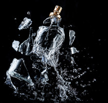 A Glass Perfume Bottle Shatters On A Black Background With Splashes And Drops Of Water