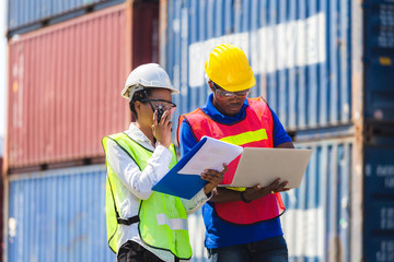 Female foreman safety vest using clipboard checklist and Worker man in hardhat holding laptop for control loading containers box from cargo