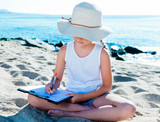 Fototapeta Natura - child girl in hat writes draws dreams with sand on seashore