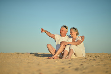 Poster - Happy elderly couple sitting on tropical beach. man pointing