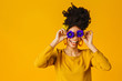 Portrait of a happy young woman holding two flowers over eyes, laughing and having fun, against yellow background