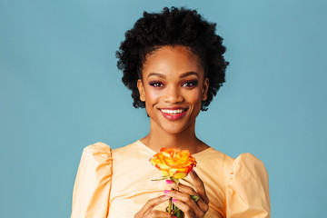 Wall Mural - Profile portrait of a happy young woman holding yellow orange rose and smiling, isolated on blue background