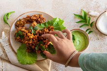 Indian Cuisine Indian Food. Pakora With Coconut Chutney Sauce Curry Leaves. Hand Of Young Indian Woman Or Child Picks Up Pakora From Plate. Authentic Vegetarian Asian Food. Travel Food By Hand