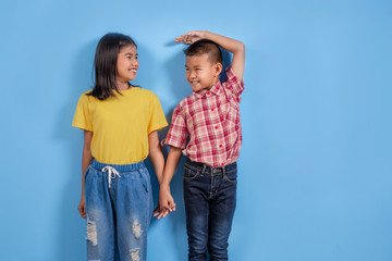 Cute Asian boy and girl measuring their height on color background