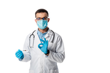 doctor in medical mask and white coat holding digital thermometer and showing ok sign isolated on white