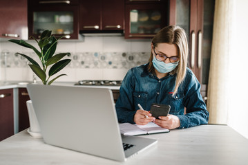 Coronavirus. Girl in mask checking social apps in phone. Woman work, learns and using laptop computer. Quarantine. Stay at home. Freelancer. Writing, typing. Communication and technology concept.