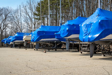 Row Of Boats Covered With Blue Shrink Wrap In Outdoor Storage Lot