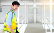 © bung - Junior engineer standing in the plant holding helmet and looking outside with copy space. Wearing safety vest. Feeling happy and smile on work. Engineering and design concept.
