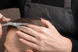 © Александр Маликов - The Barber's hand with a pair of scissors for cutting the hair of a young man. Creating a stylish men's haircut in a barbershop. Men's haircut process, brown tones close-up