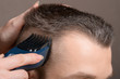 © Александр Маликов - A Barber's hand with a young man's hair clipper. Creating a stylish men's haircut in a barbershop. Men's haircut process, brown tones close-up