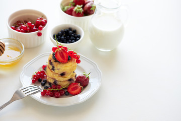 Wall Mural - Stack of pancakes (syrniki) with strawberry, red currant and blueberries on white background. Soft focus. Healthy eating concept