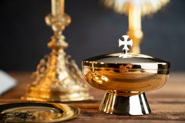 Wall Mural - Catholic religion concept. Catholic symbols composition. The Cross, monstrance,  Holy Bible and golden chalice on wooden altar and gray background. 