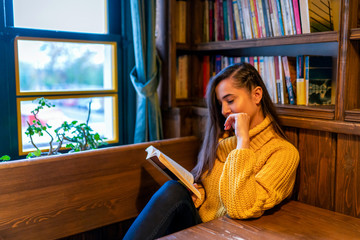 A young woman reading a book by a window