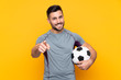 © luismolinero - Man over isolated yellow background with soccer ball and pointing to the front