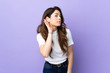 © luismolinero - Woman over isolated purple background listening to something by putting hand on the ear