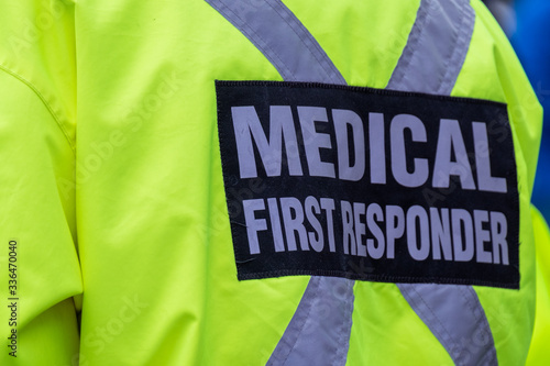 Medical first responder wearing a bright yellow uniform with the words medical first responder on their back in grey letters with a black background. There\'s a grey reflection material cross too.