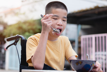 Wall Mural - Asian disabled child on wheelchair using a spoon to scoop food by themselves,Skills to practice muscle development,Special children's lifestyle,Life in the education age,Happy disability kid concept.