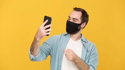 Wall Mural - Young man in sterile black face mask denim white shirt posing isolated on yellow background studio. Epidemic pandemic coronavirus 2019-ncov sars covid-19 flu virus concept. Guy hold talk on cellphone