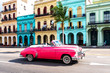 old pink convertible classic car in front of colorful houses in havana cuba