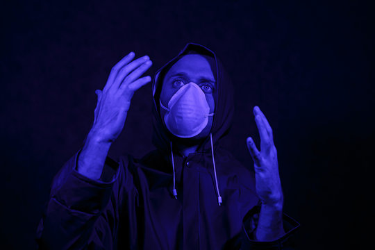 A man in a protective suit and white mask in a dark room. Halloween image concept. Virus protection. Illuminated with colored lights