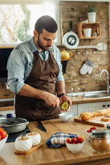 Wall Mural - Young man peeling avocado while preparing food in the kitchen.