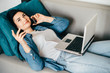 Smart working from home. Young woman laying on coach talking to business partners using smart phone and laptop. Remote work, freelance, stay home business concept
