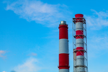 Two striped red and white factory chimneys stand side by side against a blue sky with light clouds.