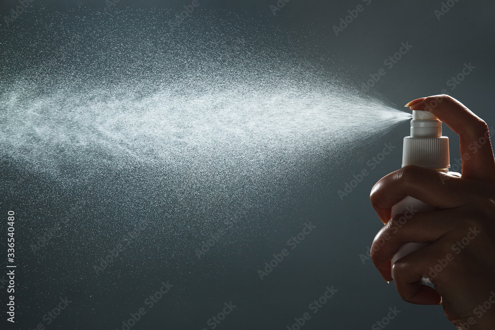 Close-up view of human hand and antiseptic spray bottle on dark background. Control Epidemic Prevention measures of coronavirus. - obrazy, fototapety, plakaty 