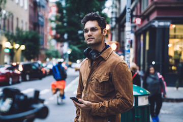 Confident ethnic young man with smartphone standing on crosswalk