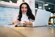 © BullRun - Portrait of cheerful female student 20s looking at camera during time for laptop e learning, happy Caucasian woman with education textbook rejoicing at desktop with modern netbook technology