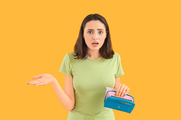 Wall Mural - Worried young woman with empty wallet on color background