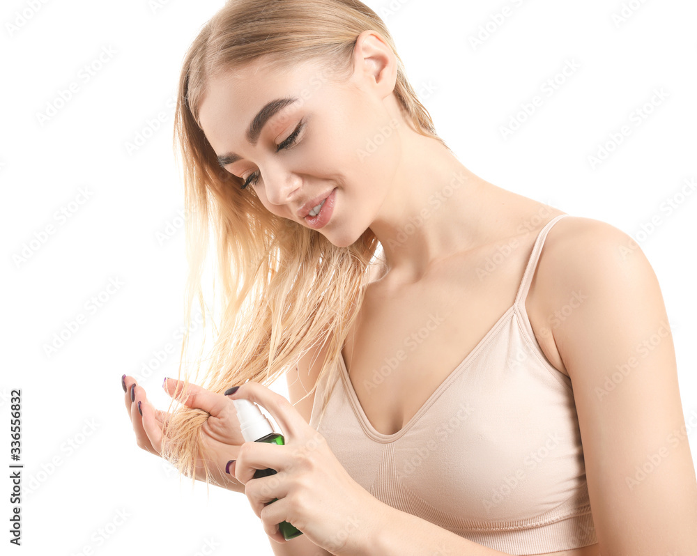 Young woman using cosmetics for hair against white background