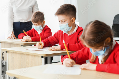 Fotografía Pupils in medical masks passing exam at school