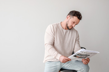 Wall Mural - Stylish man reading newspaper on light background
