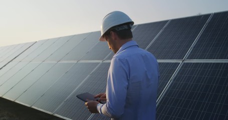 Wall Mural - an young engineer is checking with tablet an operation of sun and cleanliness on field of photovolta