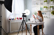 © artiemedvedev - Beauty blogger woman filming make-up asks for likes, thumbs up, subscription on camera. Influencer blonde girl live streaming cosmetics product review in studio with professional lighting equipment.
