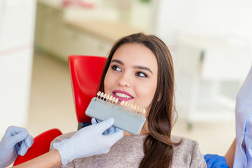 Wall Mural - Check and select the color of the teeth in the dentist chair. Dentist makes the process of treating a beautiful young red-haired girl. Selection of a tooth implant. Close-up.