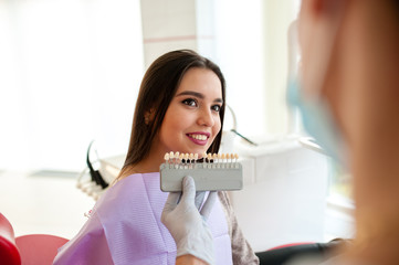 Wall Mural - Close up portrait of Young women in dentist chair, Check and select the color of the teeth. Dentist makes the process of treatment in dental clinic office.Dentist