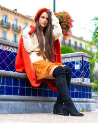 Street style, portrait of a young caucasian brunette dressed in red and with a skirt sitting in a city park