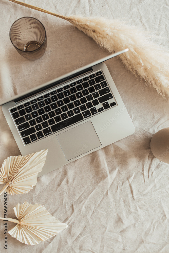 Home office desk workspace with laptop, reeds foliage, fan leaves on beige linen table cloth. Flat lay, top view. - obrazy, fototapety, plakaty 