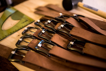 lot of handmade leather belts on a wooden board with leather tools around