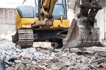 Small yellow excavator is on duty for pulling down the old buildings. Selective focus at bucket.