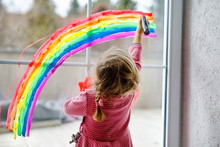 Adoralbe Little Toddler Girl With Rainbow Painted With Colorful Window Color During Pandemic Coronavirus Quarantine. Child Painting Rainbows Around The World With The Words Let's All Be Well.