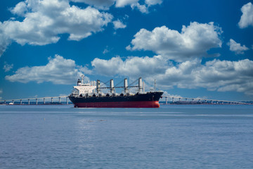 Poster - A huge old freighter on calm water by a white bridge