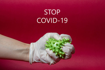 stop covid-19 hand in a medical glove tightly compresses a coronavirus on a red background with text