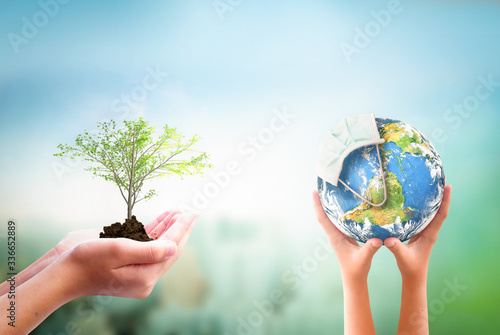 Earth Day concept: hands holding Corona virus or COVID-19 Earth globe wearing a mask  and  tree over  nature background. Elements of this image furnished by NASA
