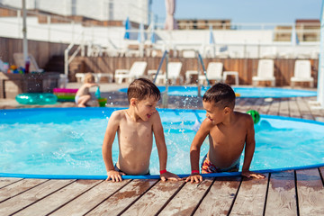 Two happy happy boys of 6-7 years splashing in the pool in the summer on vacation near the hotel. Caucasian and Asian.