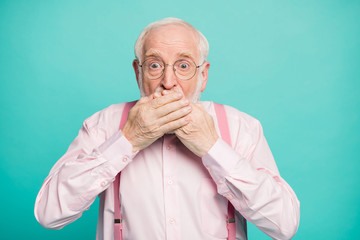 Closeup photo of crazy grandpa hiding mouth lips don't speak keeping silence big fear eyes wear specs pink shirt suspenders bow tie isolated bright teal color background